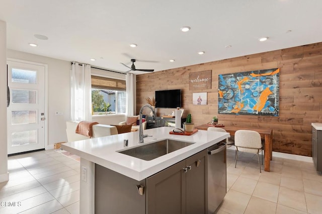 kitchen featuring an island with sink, sink, wood walls, ceiling fan, and stainless steel dishwasher