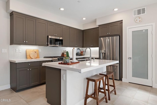 kitchen with an island with sink, stainless steel appliances, a kitchen breakfast bar, dark brown cabinetry, and sink