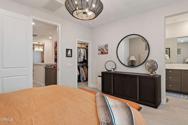 bedroom with an inviting chandelier, connected bathroom, a closet, light colored carpet, and a walk in closet