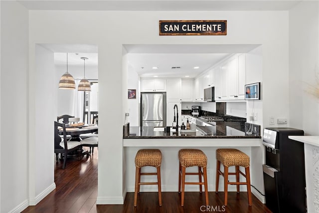 kitchen with sink, stainless steel refrigerator, hanging light fixtures, white cabinets, and dark stone counters