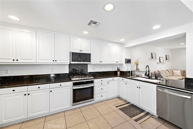 kitchen with sink, white cabinetry, appliances with stainless steel finishes, light tile patterned floors, and dark stone counters