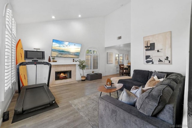 living room featuring high vaulted ceiling, a tiled fireplace, and light hardwood / wood-style floors