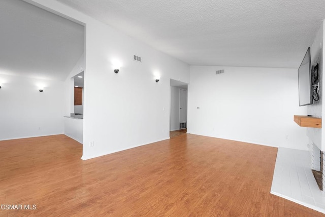 unfurnished living room featuring a textured ceiling, light hardwood / wood-style flooring, and high vaulted ceiling