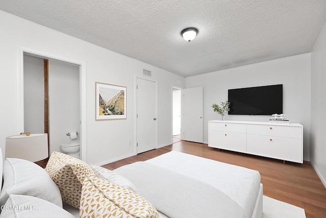 bedroom with ensuite bath, dark wood-type flooring, and a textured ceiling