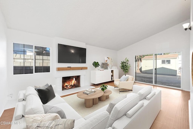 living room featuring vaulted ceiling, a brick fireplace, and light hardwood / wood-style flooring