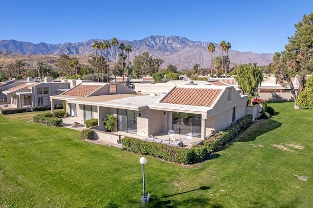 back of property with a mountain view and a lawn