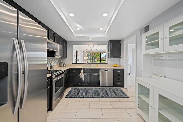 kitchen featuring sink, light tile patterned floors, appliances with stainless steel finishes, a raised ceiling, and backsplash