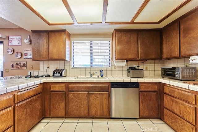 kitchen featuring stainless steel dishwasher, sink, backsplash, light tile patterned floors, and tile countertops