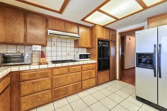 kitchen with light tile patterned flooring, tile counters, tasteful backsplash, and appliances with stainless steel finishes