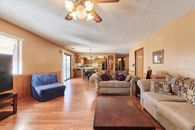 living room with ceiling fan, a textured ceiling, light hardwood / wood-style flooring, and wood walls