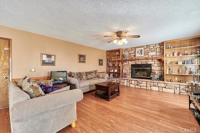 living room featuring built in features, light wood-type flooring, a fireplace, and a textured ceiling