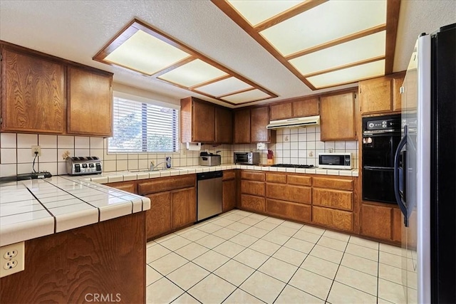 kitchen with sink, backsplash, tile counters, light tile patterned floors, and stainless steel appliances