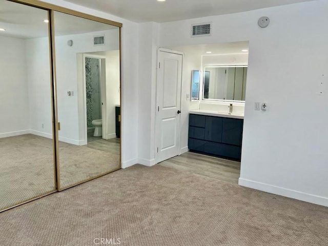 unfurnished bedroom featuring light colored carpet, a closet, sink, and connected bathroom