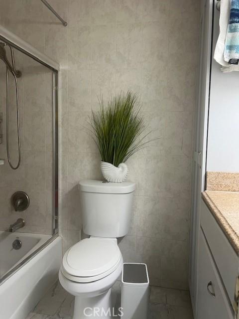 full bathroom with toilet, vanity, tile walls, and bath / shower combo with glass door