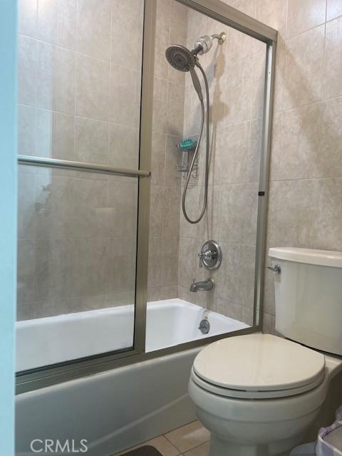 bathroom with toilet, combined bath / shower with glass door, and tile patterned floors