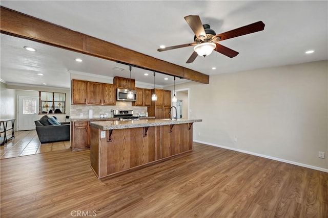 kitchen with pendant lighting, a large island, appliances with stainless steel finishes, light stone countertops, and light hardwood / wood-style floors