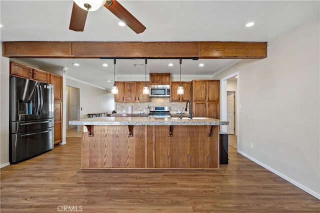 kitchen with appliances with stainless steel finishes, wood-type flooring, a kitchen breakfast bar, hanging light fixtures, and a large island