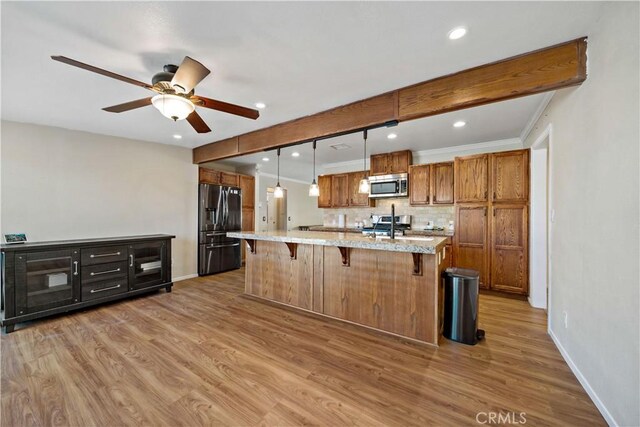 kitchen with appliances with stainless steel finishes, wood-type flooring, tasteful backsplash, a kitchen breakfast bar, and hanging light fixtures