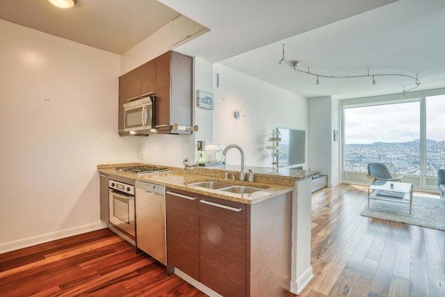 kitchen featuring dark wood-type flooring, dishwasher, oven, light stone countertops, and sink