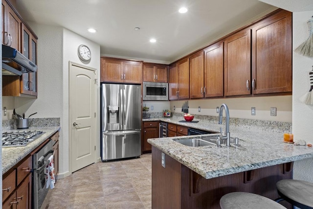 kitchen featuring kitchen peninsula, sink, light stone counters, a breakfast bar area, and stainless steel appliances