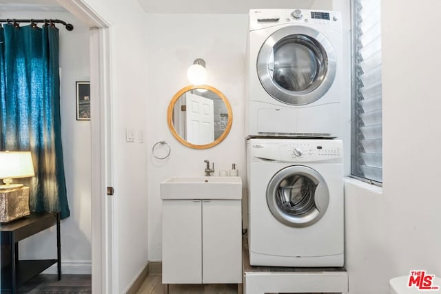 clothes washing area featuring stacked washer / dryer, wood-type flooring, and sink