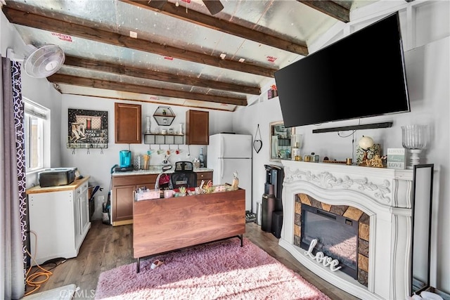 interior space with wood finished floors, beamed ceiling, ceiling fan, and a glass covered fireplace