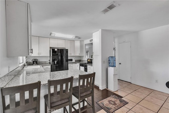 kitchen featuring black appliances, white cabinetry, sink, kitchen peninsula, and light tile patterned flooring