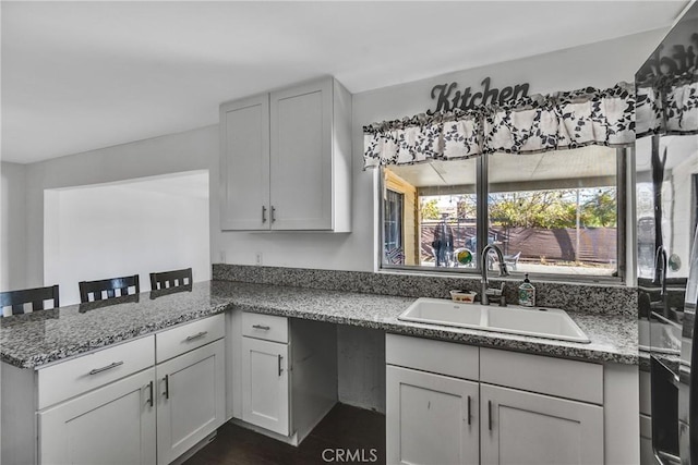 kitchen with stone counters, a kitchen breakfast bar, kitchen peninsula, and sink