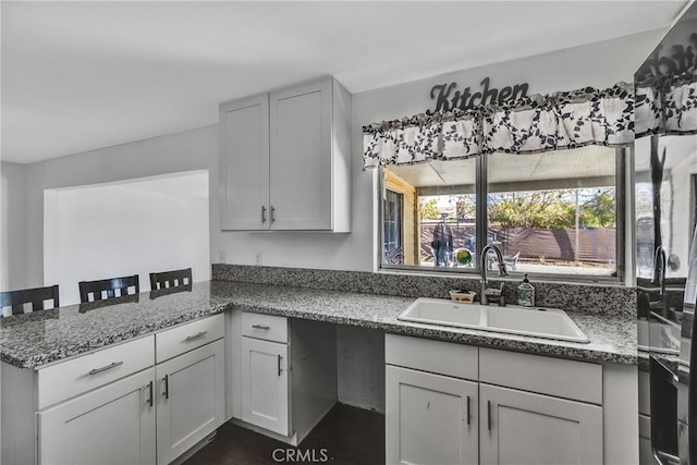 kitchen featuring stone countertops, a peninsula, and a sink