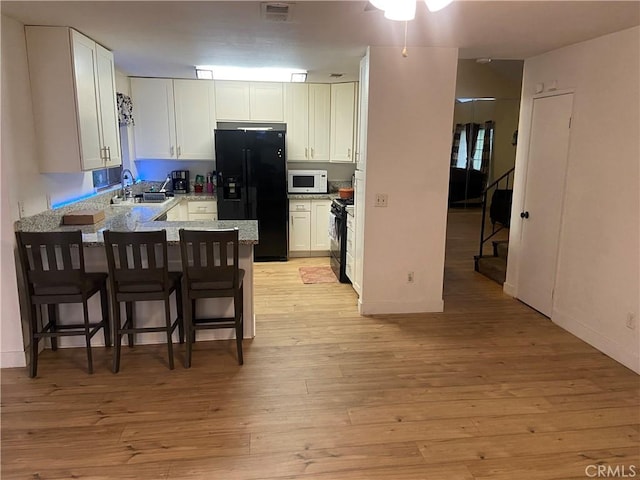 kitchen with a peninsula, visible vents, black appliances, a sink, and light wood finished floors