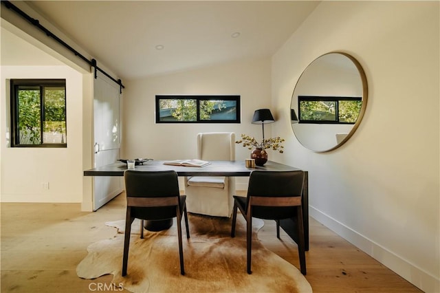 dining area featuring light hardwood / wood-style floors, lofted ceiling, and a barn door