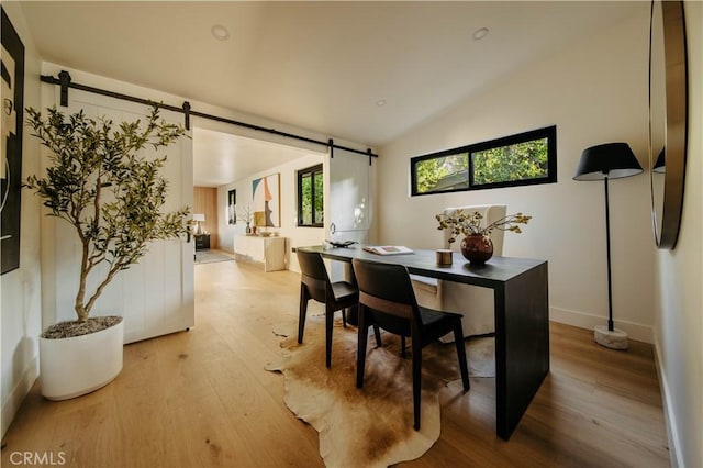 dining room featuring light wood-type flooring, a barn door, and vaulted ceiling