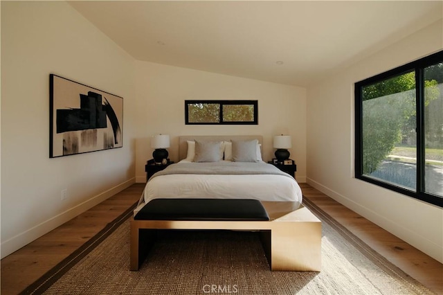 bedroom featuring vaulted ceiling, multiple windows, and hardwood / wood-style floors