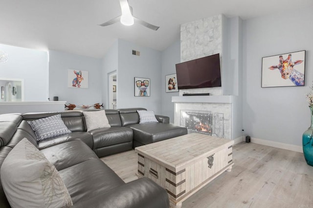 living room featuring ceiling fan, light hardwood / wood-style flooring, a stone fireplace, and vaulted ceiling