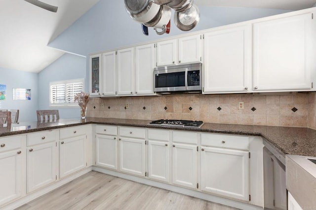 kitchen featuring white cabinetry, dark stone counters, backsplash, stainless steel appliances, and lofted ceiling