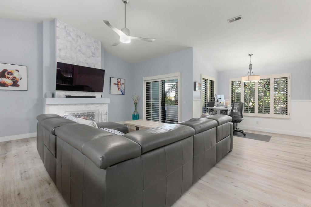 living room featuring ceiling fan, a large fireplace, light hardwood / wood-style flooring, and vaulted ceiling