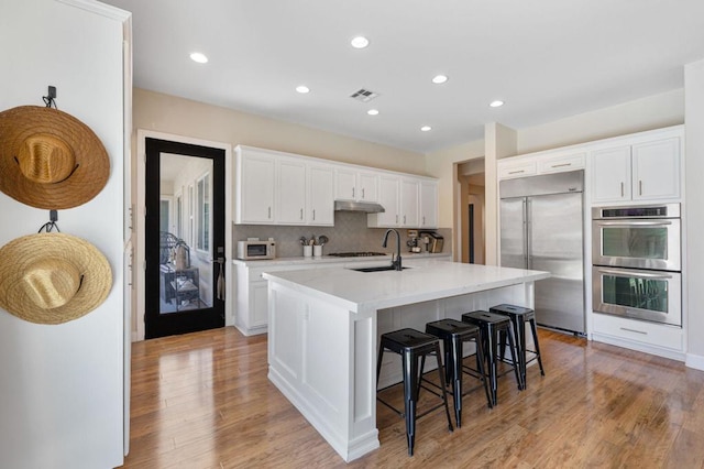 kitchen featuring a kitchen bar, white cabinetry, a center island with sink, and stainless steel appliances