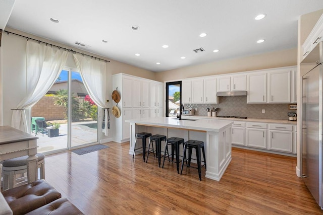 kitchen featuring white cabinets, an island with sink, sink, light wood-type flooring, and gas cooktop