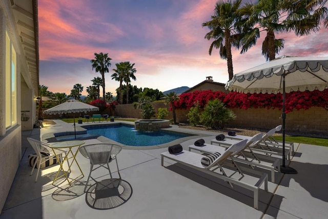 pool at dusk with an in ground hot tub and a patio