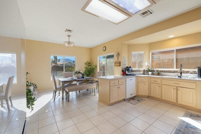 kitchen featuring light tile patterned floors, kitchen peninsula, light brown cabinets, white dishwasher, and hanging light fixtures