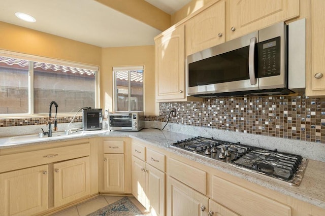 kitchen with light tile patterned floors, stainless steel appliances, light brown cabinets, tasteful backsplash, and sink