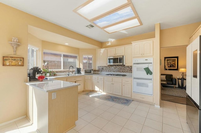 kitchen with kitchen peninsula, decorative backsplash, sink, appliances with stainless steel finishes, and light tile patterned floors