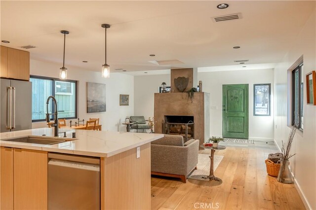 kitchen with decorative light fixtures, a center island with sink, stainless steel dishwasher, sink, and light wood-type flooring