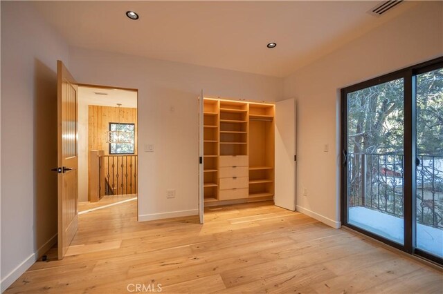 unfurnished bedroom featuring access to outside, a walk in closet, light wood-type flooring, and a closet