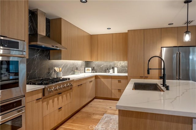 kitchen with appliances with stainless steel finishes, wall chimney exhaust hood, decorative light fixtures, light brown cabinets, and sink