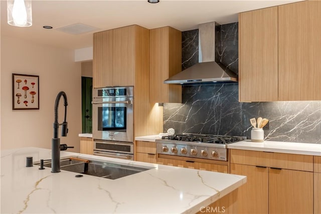 kitchen with stainless steel gas stovetop, tasteful backsplash, light brown cabinetry, light stone countertops, and wall chimney range hood