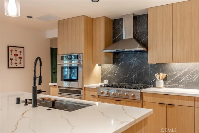 kitchen with modern cabinets, light brown cabinetry, stainless steel appliances, wall chimney exhaust hood, and decorative backsplash