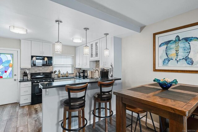 kitchen featuring decorative light fixtures, black appliances, kitchen peninsula, a breakfast bar area, and white cabinets