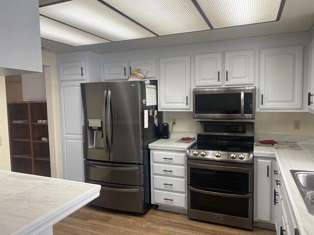 kitchen featuring appliances with stainless steel finishes, dark wood-type flooring, white cabinetry, sink, and tile countertops