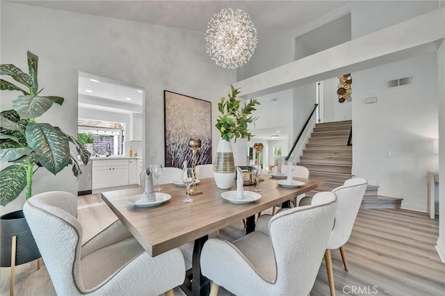 dining space with a high ceiling, light hardwood / wood-style flooring, sink, and an inviting chandelier